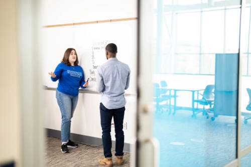 two students have a discussion in front of a white board